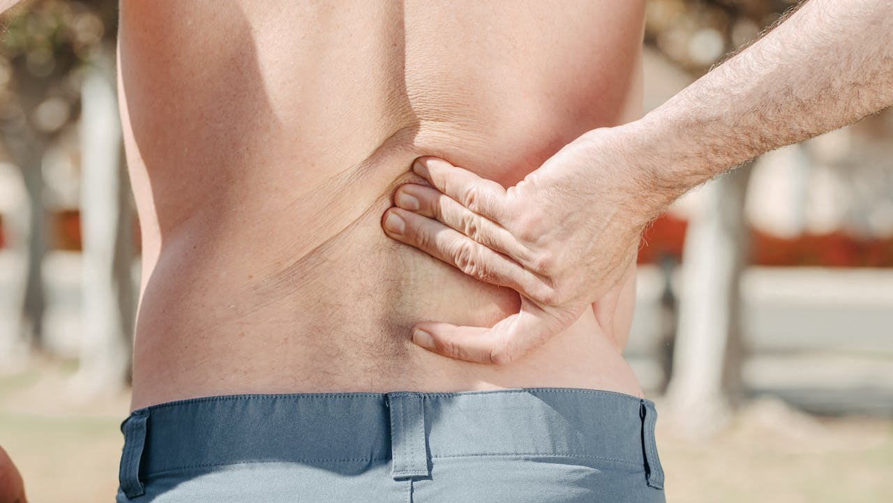 Services-03 Close-up of a man holding his lower back in pain, possibly indicating discomfort or injury.